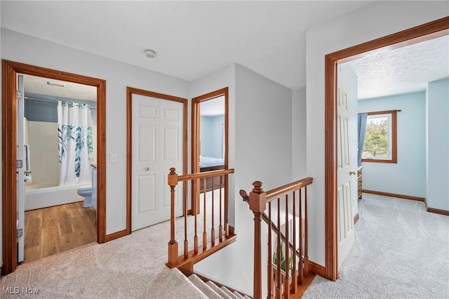 hall with an upstairs landing, baseboards, carpet floors, and a textured ceiling