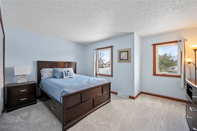 bedroom with visible vents, light colored carpet, a textured ceiling, and baseboards