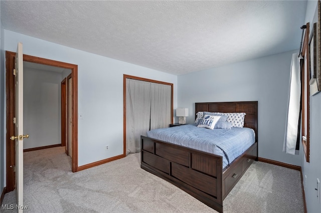 bedroom with a closet, baseboards, a textured ceiling, and light colored carpet