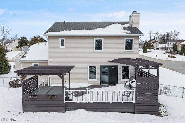 snow covered house featuring a wooden deck, a chimney, and fence