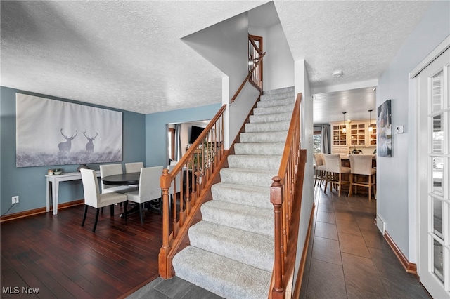 staircase with a textured ceiling, baseboards, and wood finished floors