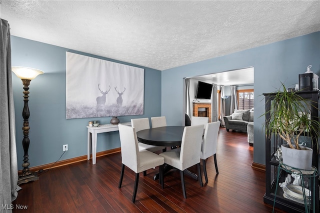 dining room with a brick fireplace, a textured ceiling, baseboards, and wood-type flooring