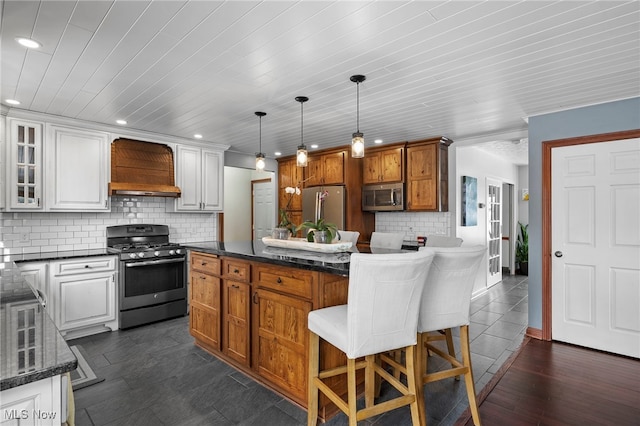 kitchen with stainless steel appliances, custom range hood, white cabinets, a kitchen breakfast bar, and backsplash