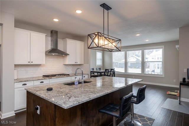 kitchen featuring white cabinetry, an island with sink, sink, and wall chimney exhaust hood