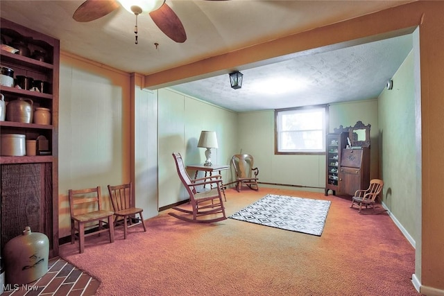 living area featuring beamed ceiling, ceiling fan, carpet floors, and a textured ceiling