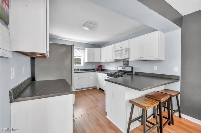 kitchen with appliances with stainless steel finishes, white cabinets, a kitchen breakfast bar, kitchen peninsula, and light hardwood / wood-style flooring