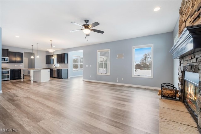 living room featuring ceiling fan, plenty of natural light, a stone fireplace, and light hardwood / wood-style flooring