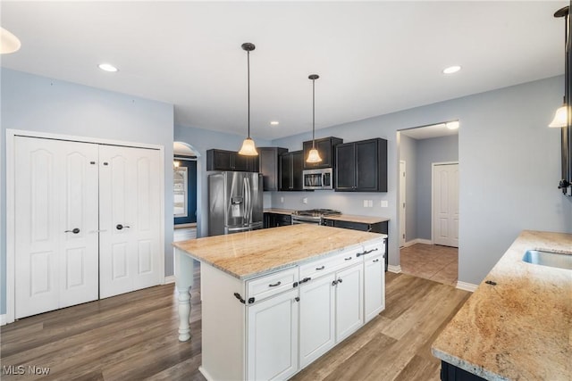 kitchen featuring stainless steel appliances, decorative light fixtures, a center island, and light stone countertops