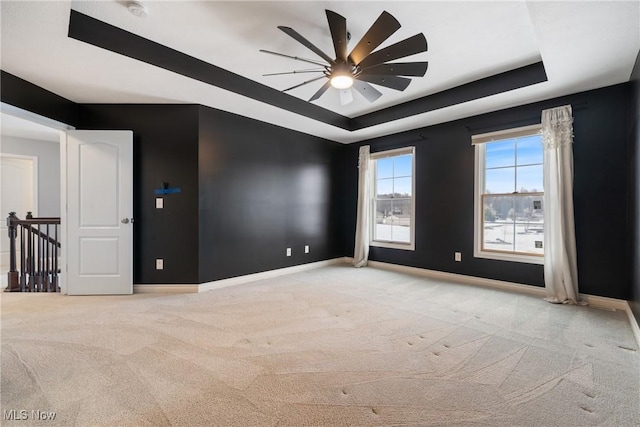 carpeted empty room with a raised ceiling and ceiling fan