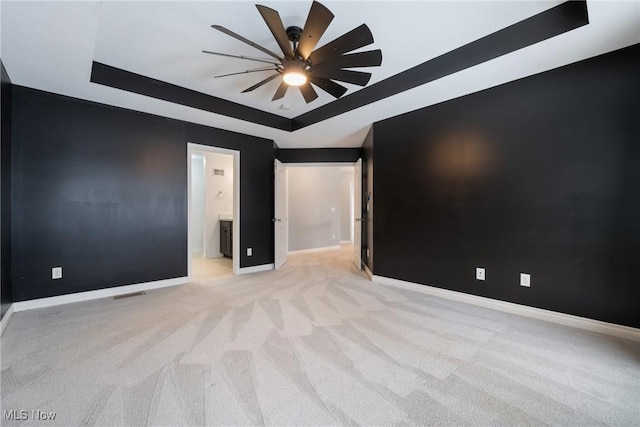 carpeted empty room with ceiling fan and a raised ceiling