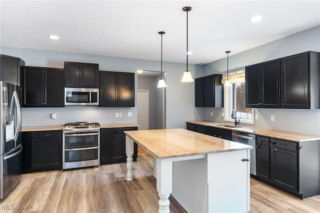 kitchen with decorative light fixtures, sink, a center island, stainless steel appliances, and light hardwood / wood-style flooring