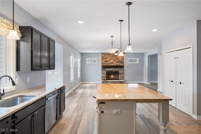 kitchen with sink, dishwasher, light stone countertops, a kitchen island, and decorative light fixtures