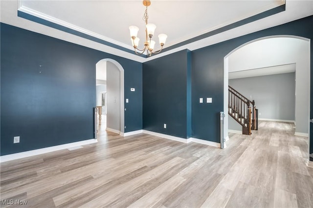 spare room with light hardwood / wood-style floors, a raised ceiling, and a chandelier