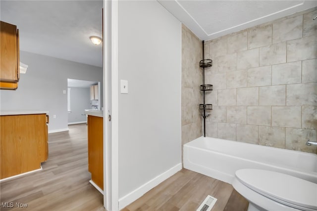 full bathroom with hardwood / wood-style flooring, vanity, tiled shower / bath, and toilet