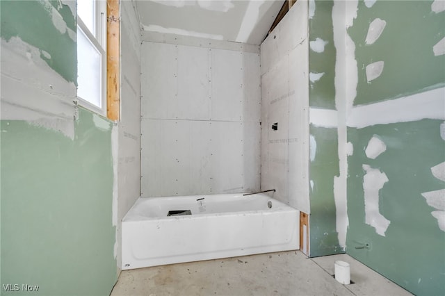 bathroom with a tub to relax in and concrete flooring