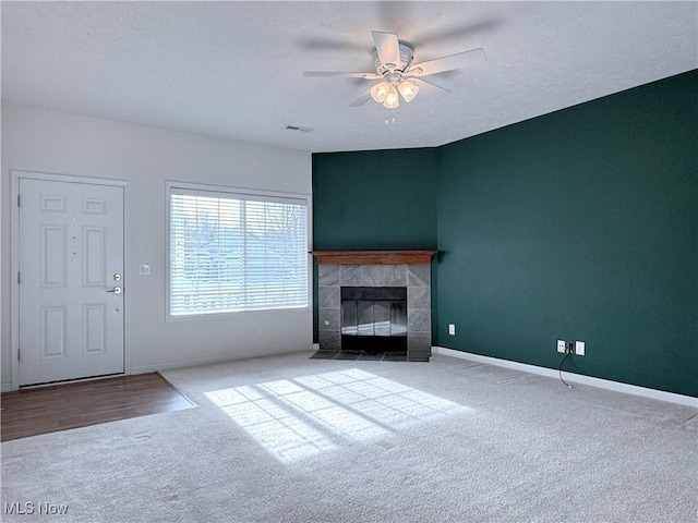 unfurnished living room with ceiling fan, a tiled fireplace, light carpet, and a textured ceiling