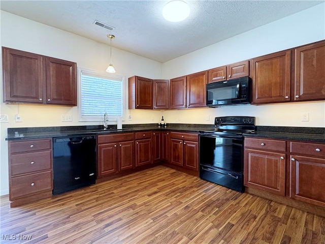 kitchen featuring pendant lighting, wood-type flooring, sink, black appliances, and a textured ceiling