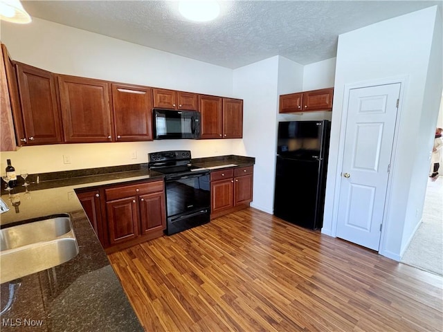 kitchen featuring sink, dark wood-type flooring, black appliances, and a textured ceiling