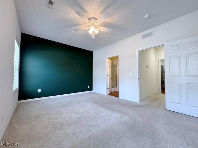 unfurnished bedroom with ceiling fan, light colored carpet, and a textured ceiling