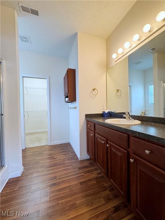 bathroom featuring vanity, wood-type flooring, a textured ceiling, and walk in shower