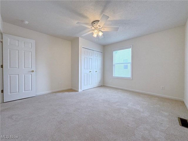 unfurnished bedroom with ceiling fan, light carpet, a closet, and a textured ceiling