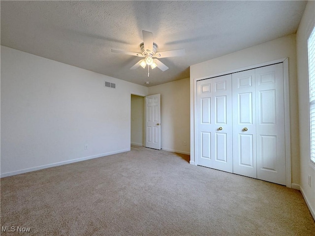 unfurnished bedroom featuring ceiling fan, light colored carpet, a closet, and a textured ceiling