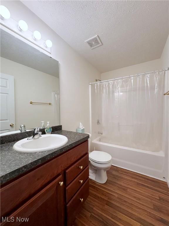 full bathroom featuring shower / tub combo, vanity, wood-type flooring, a textured ceiling, and toilet