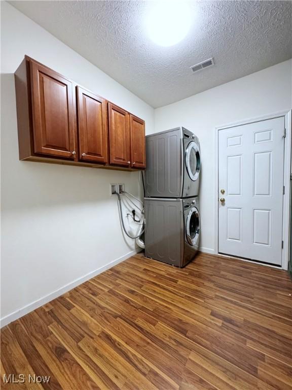 clothes washing area with cabinets, dark wood-type flooring, stacked washer and clothes dryer, and a textured ceiling