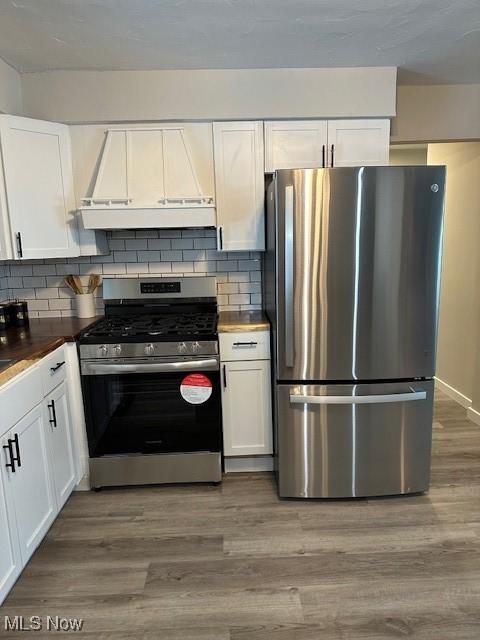 kitchen with white cabinetry, wood-type flooring, stainless steel appliances, and custom range hood