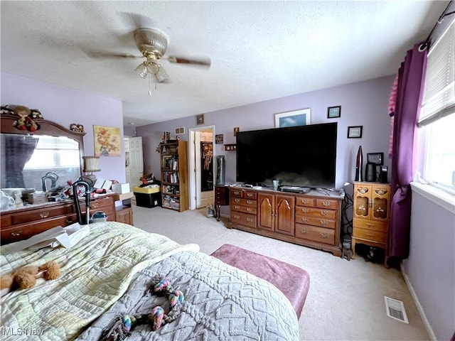 bedroom featuring ceiling fan, light colored carpet, multiple windows, and a textured ceiling