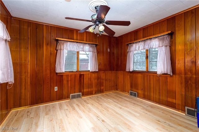 empty room with ceiling fan, wooden walls, and light hardwood / wood-style floors