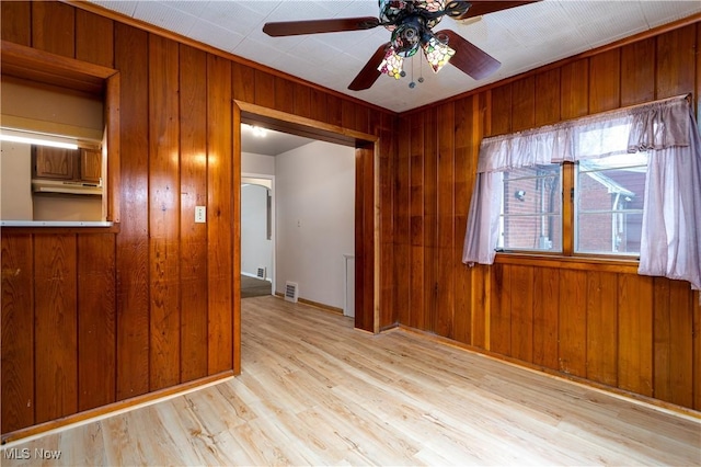 unfurnished room with ceiling fan, light hardwood / wood-style floors, and wood walls