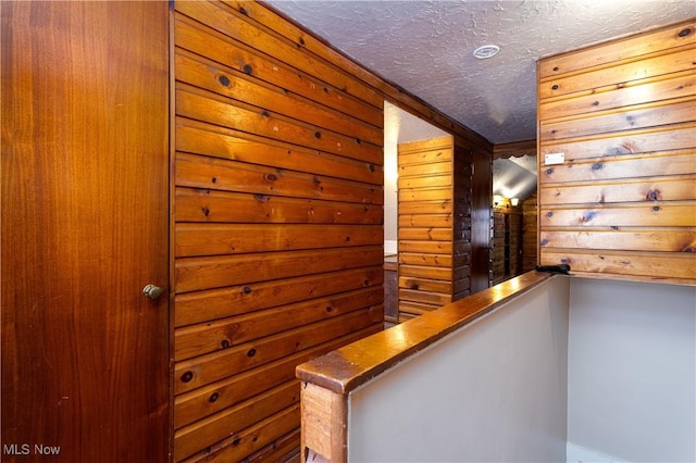 hall featuring wooden walls and a textured ceiling