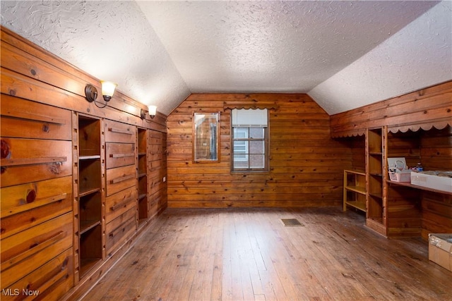 bonus room with hardwood / wood-style flooring, wooden walls, vaulted ceiling, and a textured ceiling