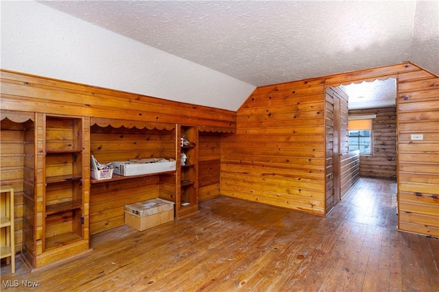 unfurnished bedroom with hardwood / wood-style flooring, lofted ceiling, a textured ceiling, and wood walls