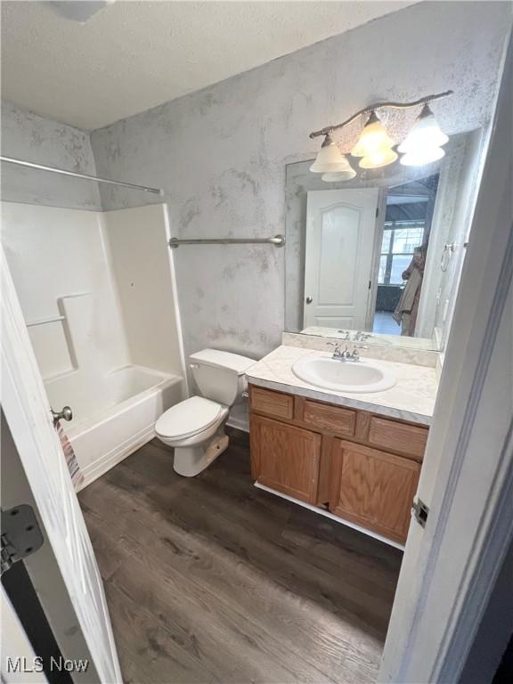 full bathroom featuring hardwood / wood-style flooring, vanity,  shower combination, toilet, and a textured ceiling