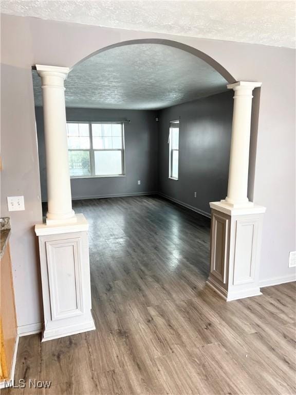 unfurnished living room featuring hardwood / wood-style floors, decorative columns, and a textured ceiling