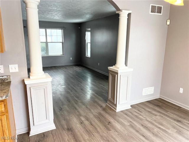 unfurnished living room featuring decorative columns, wood-type flooring, and a textured ceiling