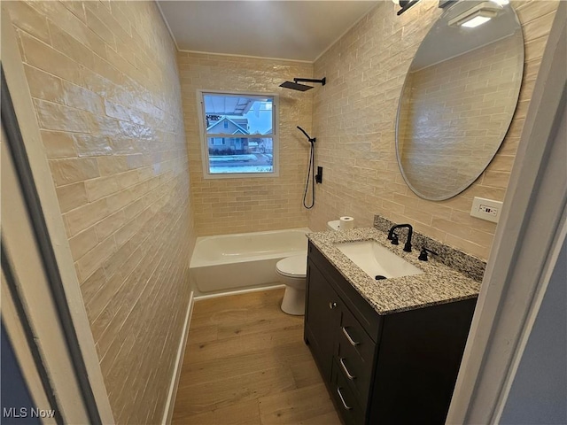 full bathroom with hardwood / wood-style flooring, tile walls, tiled shower / bath combo, vanity, and toilet