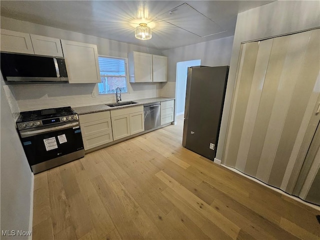 kitchen with appliances with stainless steel finishes, light hardwood / wood-style floors, sink, and white cabinets