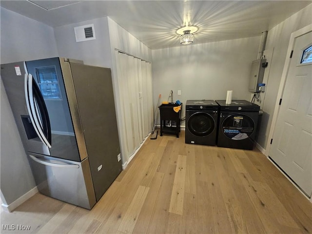 clothes washing area featuring washing machine and dryer, light hardwood / wood-style floors, and electric panel