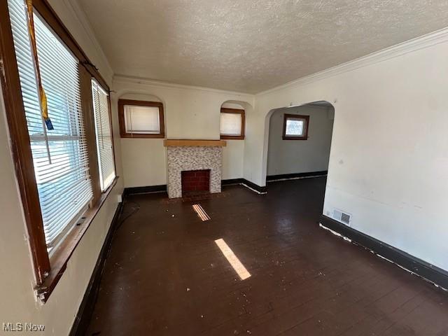 unfurnished living room with a tiled fireplace, crown molding, dark wood-type flooring, and a textured ceiling