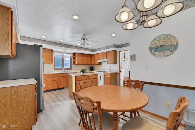 dining space with sink, ceiling fan with notable chandelier, light hardwood / wood-style floors, and a textured ceiling