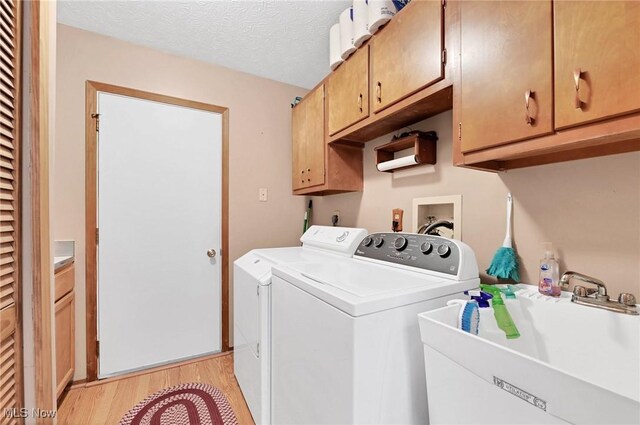 washroom featuring washing machine and clothes dryer, sink, cabinets, a textured ceiling, and light hardwood / wood-style flooring