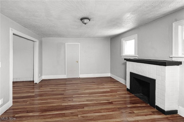 unfurnished living room with a tiled fireplace, dark hardwood / wood-style floors, and a textured ceiling