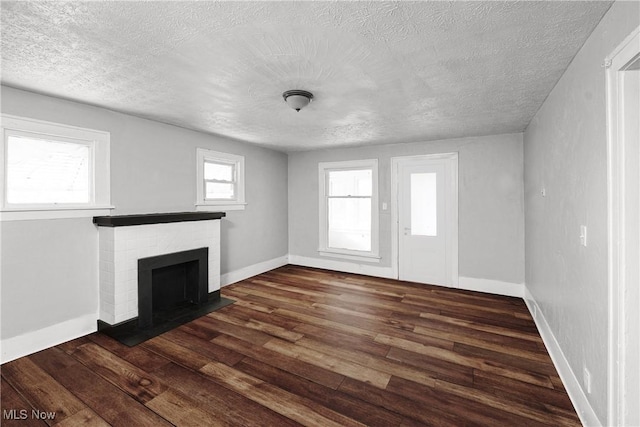 unfurnished living room featuring dark hardwood / wood-style flooring, a brick fireplace, and a textured ceiling