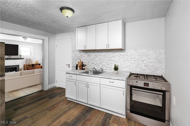 kitchen with stainless steel gas range, sink, white cabinetry, dark hardwood / wood-style floors, and a premium fireplace