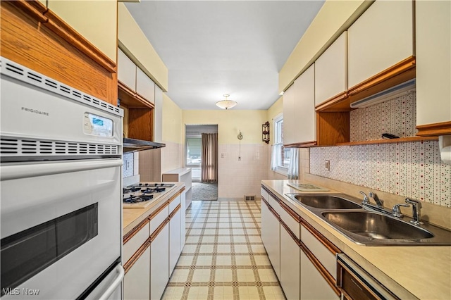 kitchen with white cabinetry, sink, tile walls, and white appliances