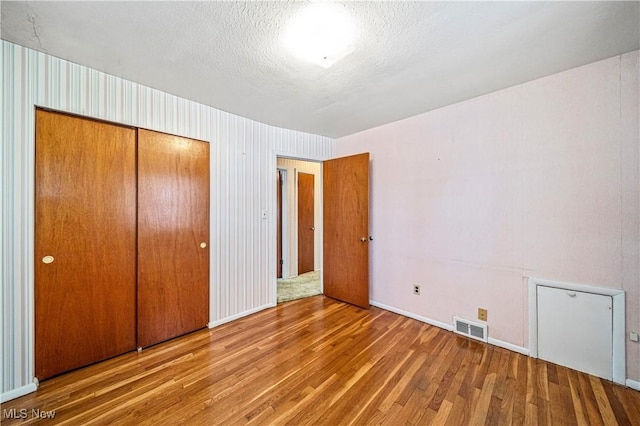 unfurnished bedroom featuring hardwood / wood-style floors, a closet, and a textured ceiling