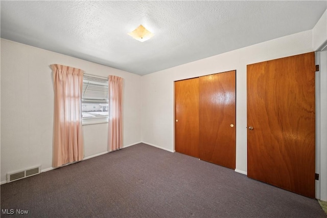 unfurnished bedroom with two closets, a textured ceiling, and dark colored carpet